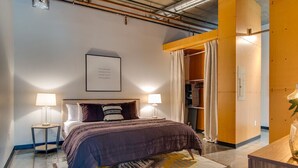 Een moderne hotelkamer met een bed, nachtlampjes, een lijst met een citaat aan de muur en een kast met gordijn.
