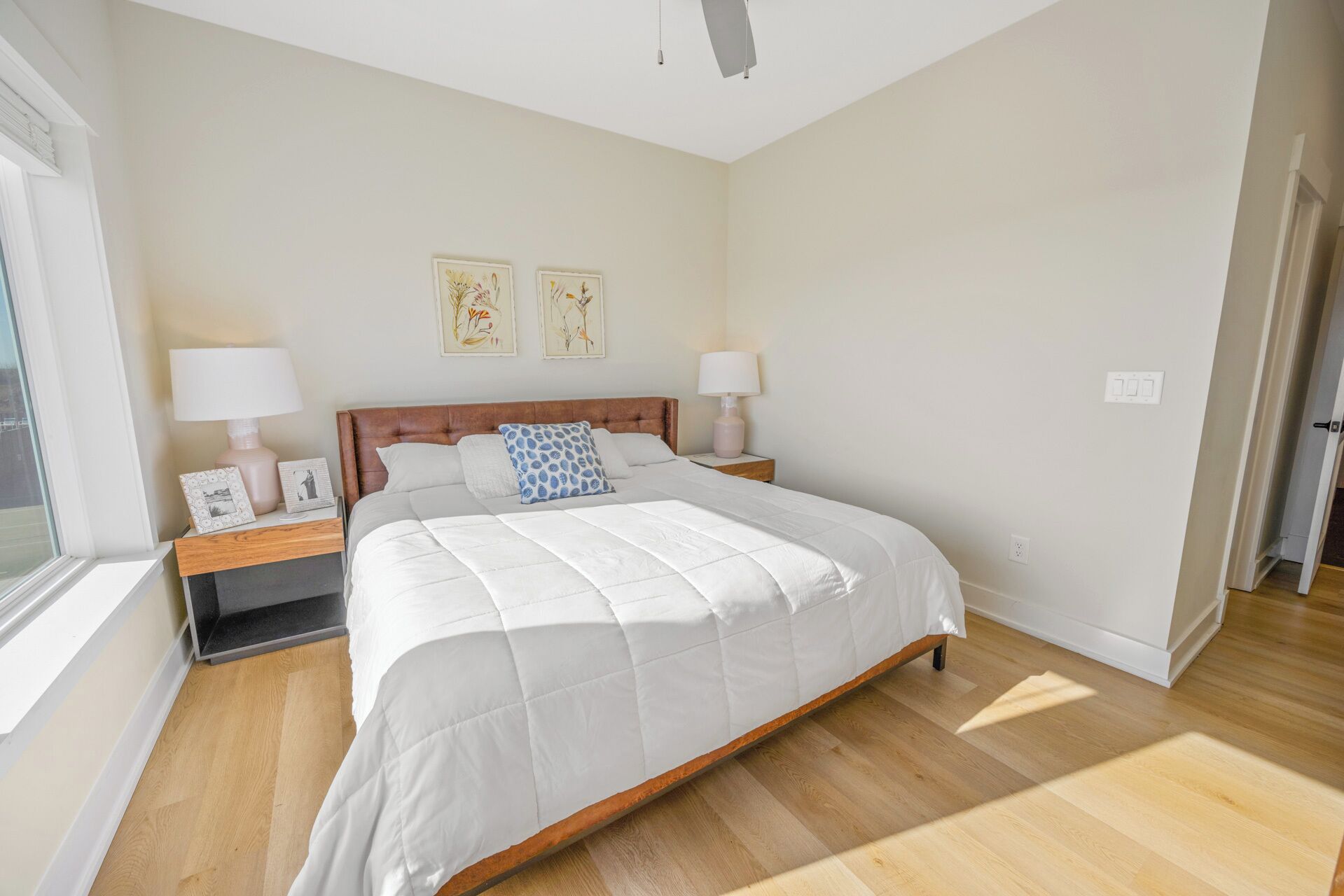 A bedroom with a wooden bed, two bedside tables with lamps, a window, and two wall-mounted artworks.