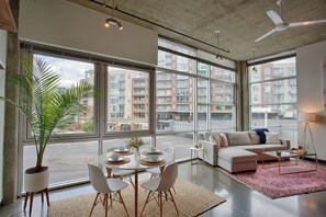 A modern living room with a dining area, large windows, and a view of a cityscape. - Sleep 6! Stylish Loft Near Broadway! (Nashville)