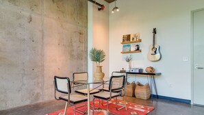 A dining area with a glass table, four chairs, a red patterned rug, a potted plant, and wall-mounted guitars. - Perfect Gulch Pad for Corporate Guests! (Nashville)