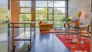 A spacious room with a large window, a sofa, a dining table with chairs, and a cart. - Perfect Gulch Pad for Corporate Guests! (Nashville)