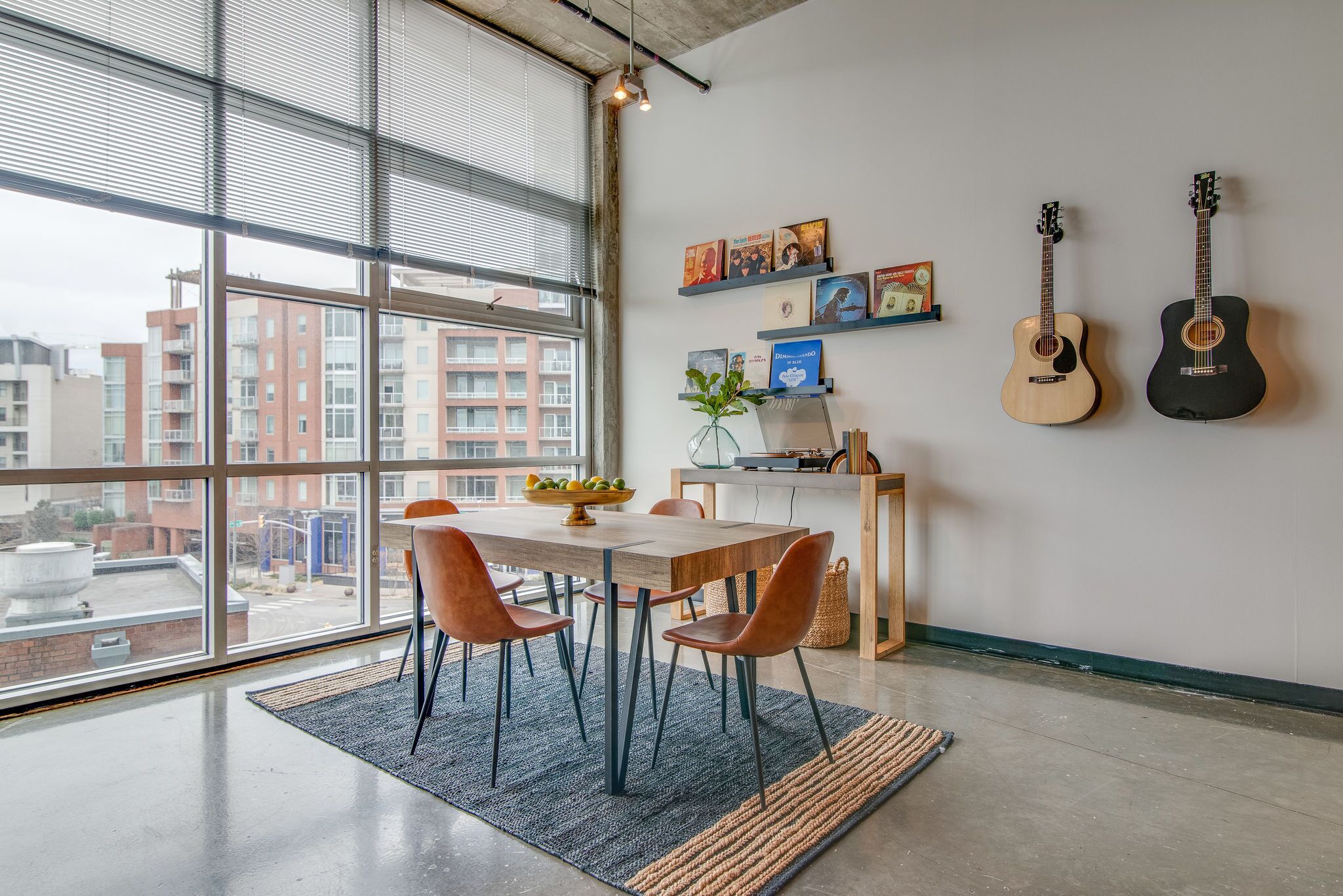 A dining area with a large window, a table with chairs, and two guitars on the wall.