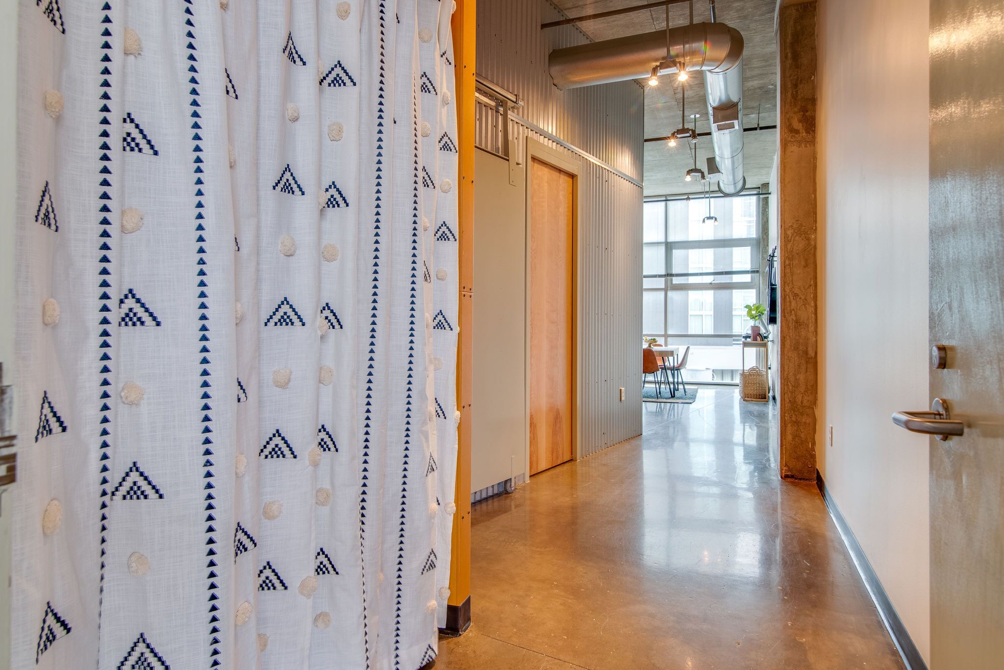 A hallway with a patterned curtain, a wooden door, and a view into a room with a table and chairs.