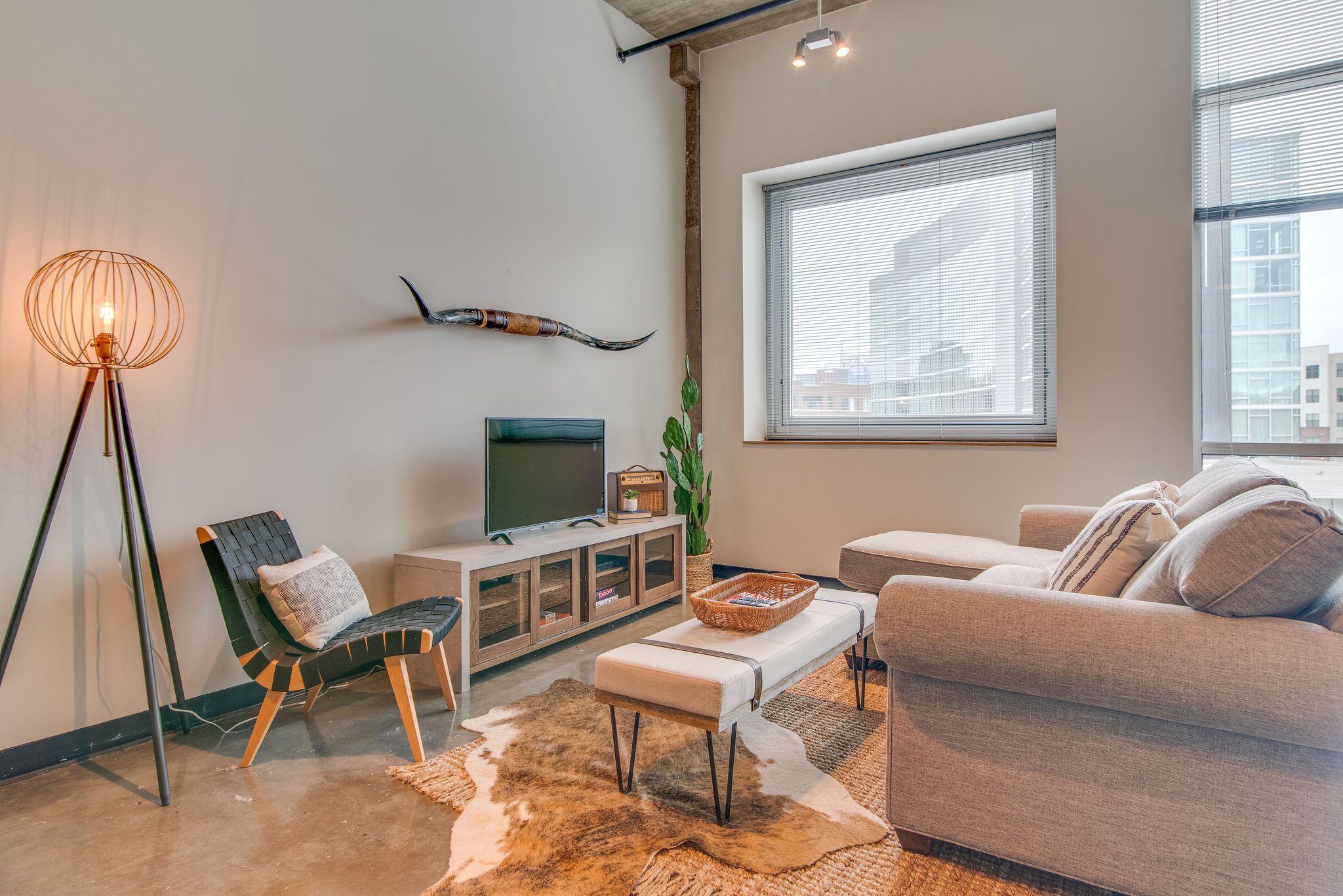 A modern living room with a sofa, a chair, a TV, a lamp, and a large window.