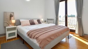 Une chambre moderne avec un grand lit, une table de chevet avec une lampe, une vue sur la ville par la fenêtre et un panorama urbain visible à l’extérieur.