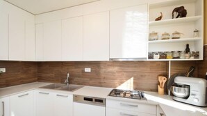 Une cuisine moderne avec des meubles blancs, un pare-feu en bois, un lave-vaisselle encastré, une cuisinière à gaz et une machine à café.