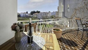 Un balcon avec une table dressée pour deux personnes, une bouteille de vin et un vase de fleurs.