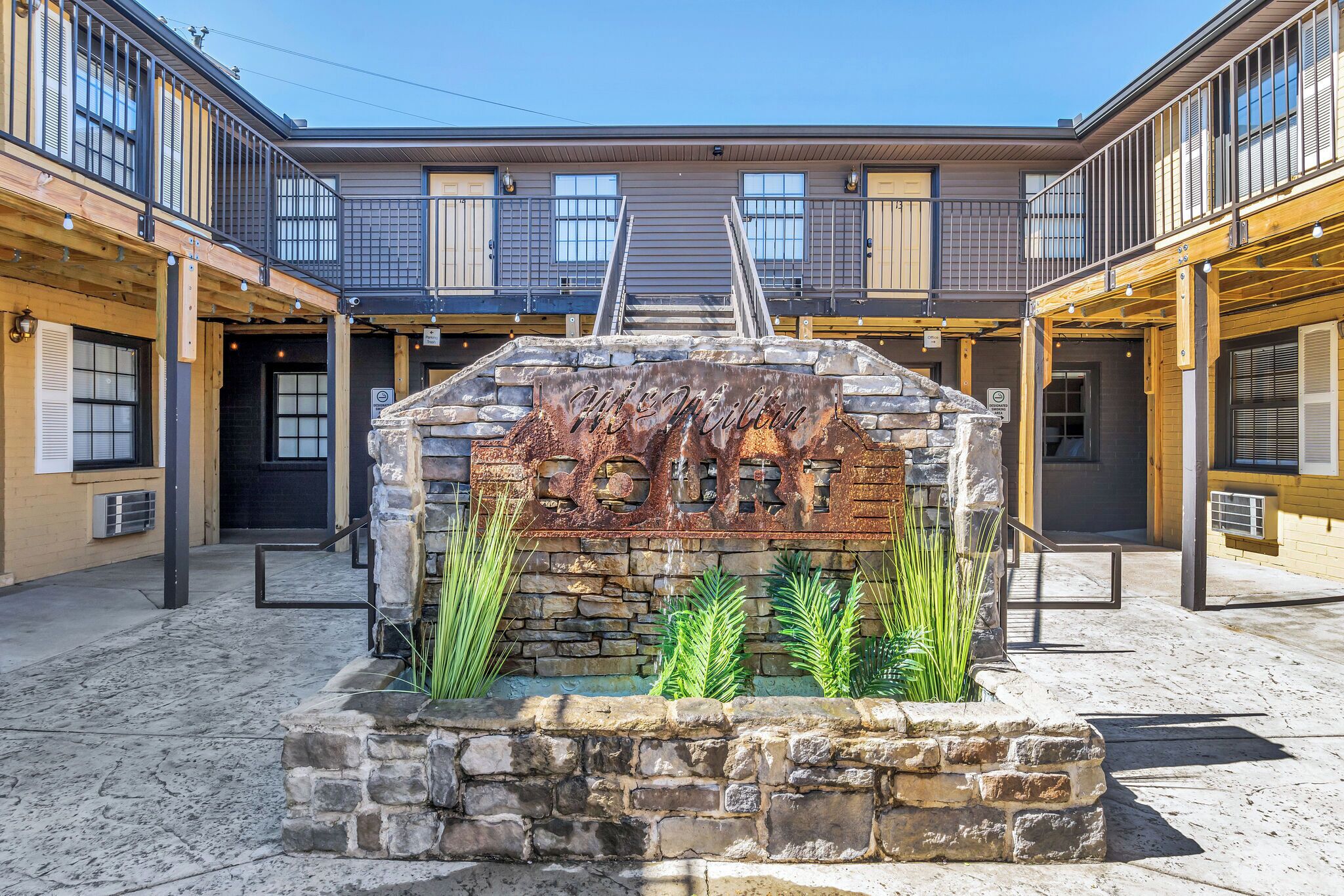A courtyard with a stone fountain, wooden benches, and a staircase leading to a building with balconies.