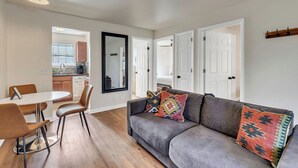 Ein modernes Wohnzimmer mit einem grauen Sofa, einem Esstisch mit Stühlen und einer Küche im Hintergrund.