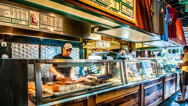 Mostrador de restaurante con un menú, una parrilla y una persona cocinando.