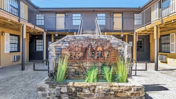 A courtyard with a stone fountain, wooden benches, and a staircase leading to a building with balconies.
