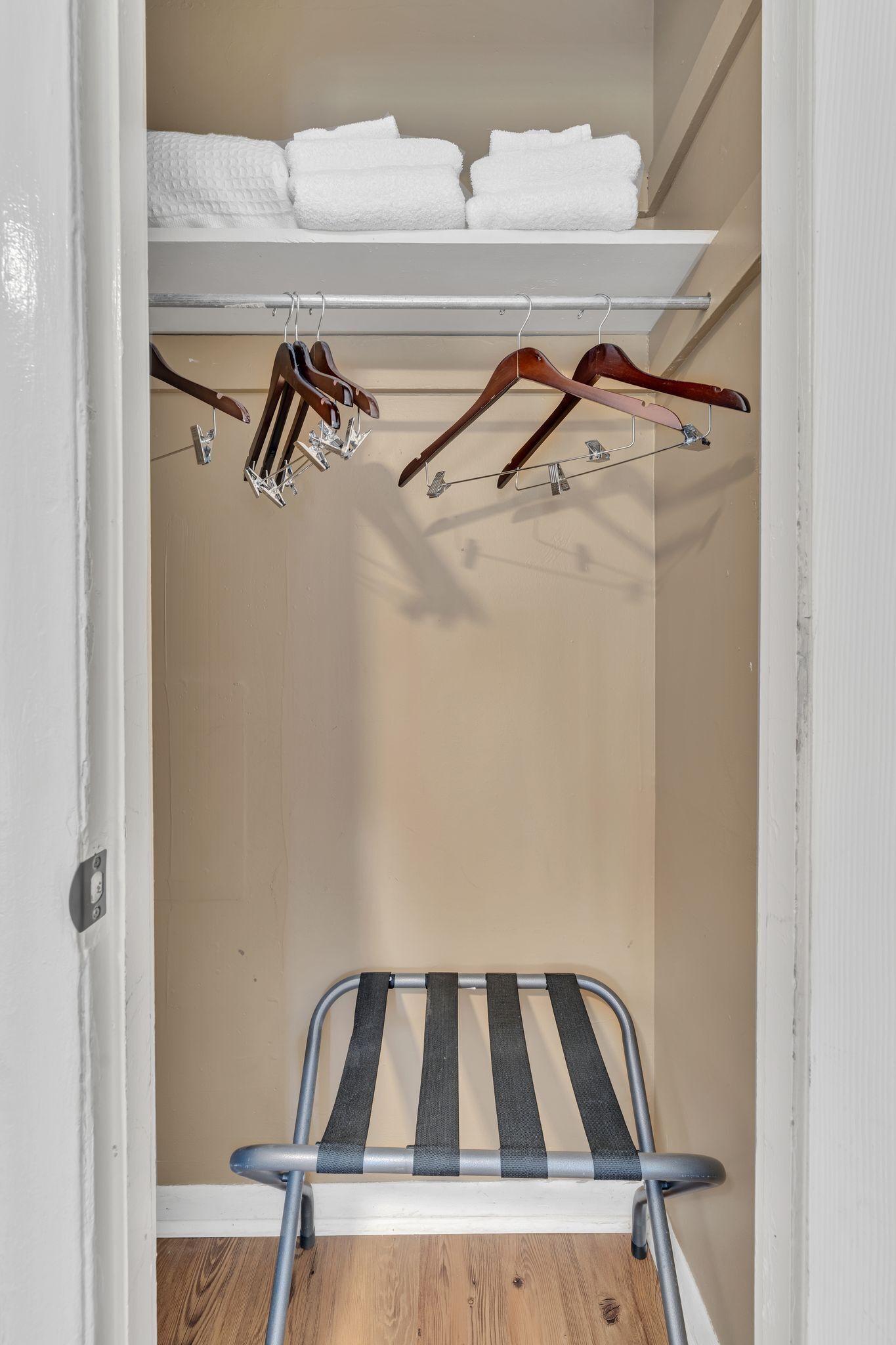 A walk-in closet with a metal drying rack, wooden hangers, and neatly folded white towels on a shelf.