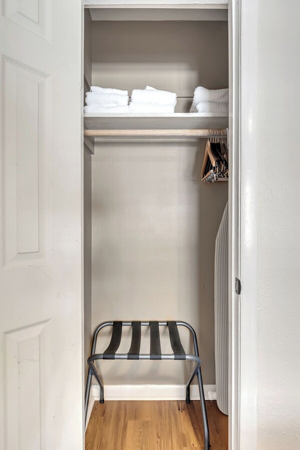 A walk-in closet with a metal bench, shelves with folded towels, and a wooden rack with hanging items.