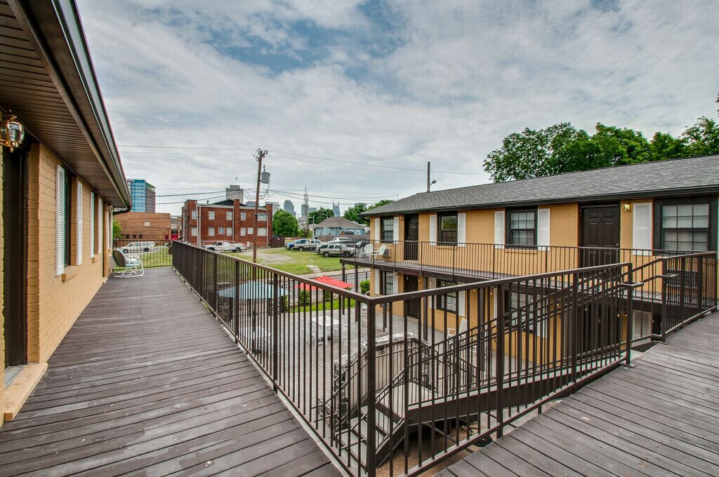 A wooden deck with a metal railing, a building with a brown facade, and a clear sky.