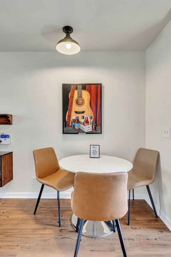 Un comedor con una mesa redonda, dos sillas, un ventilador de techo y un cuadro colgado en la pared que muestra una guitarra.