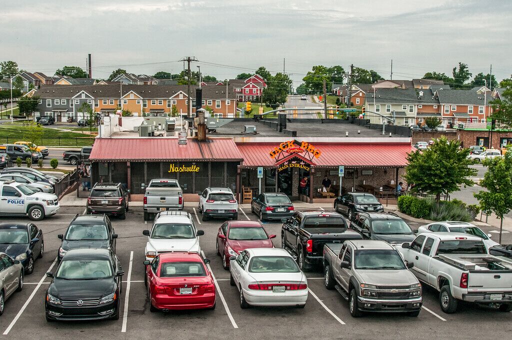 Ein Parkplatz mit mehreren Autos und einem Gebäude mit rotem Dach sowie einem Schild mit der Aufschrift 'Nashville'.