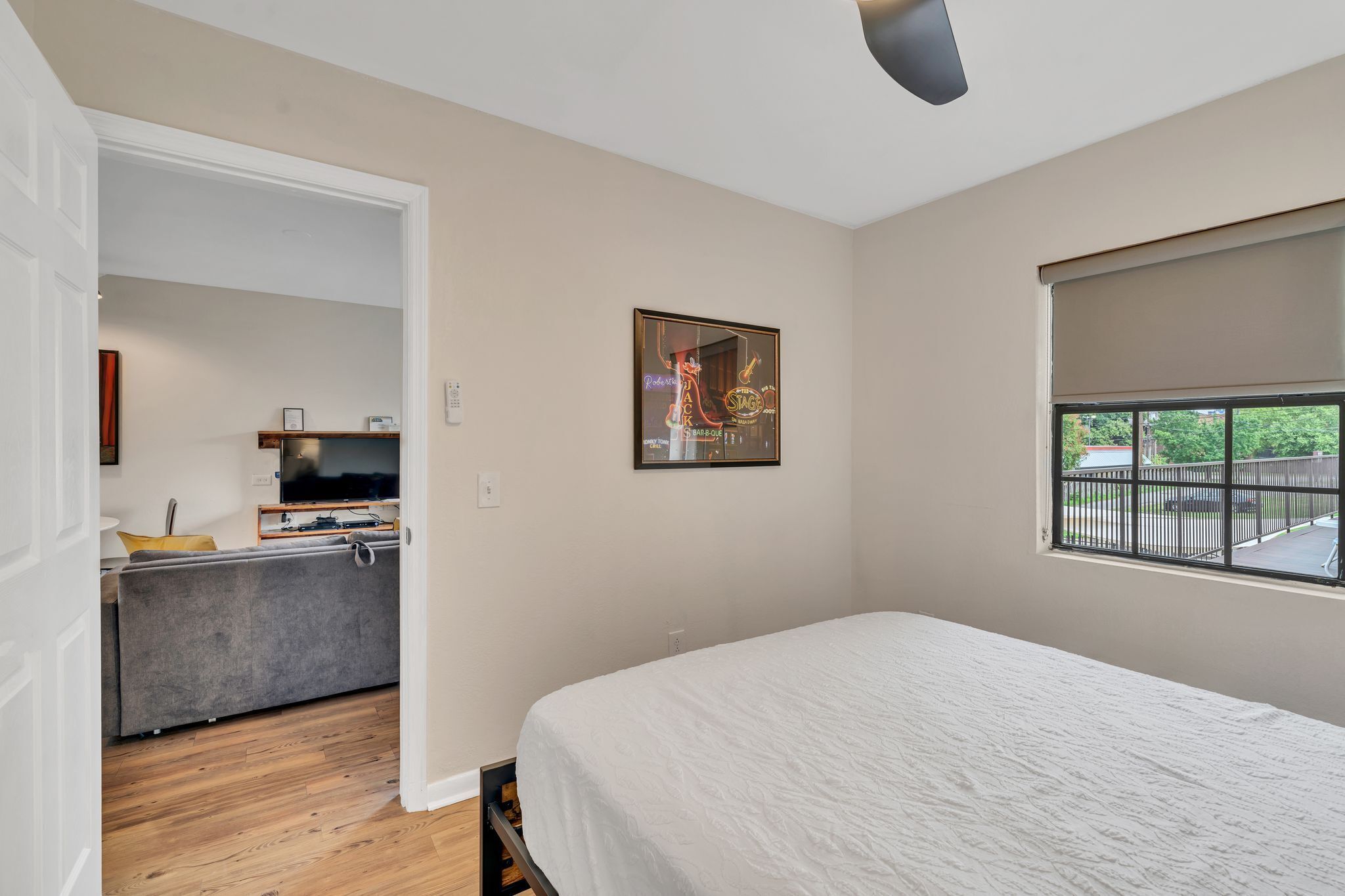 Un dormitorio con cama, ventana con vista, un cuadro en la pared y una kitchenette al fondo.