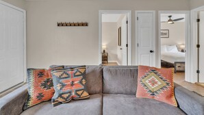 Un salon avec un canapé gris, deux coussins décoratifs à motifs et un porte-manteau en bois.
