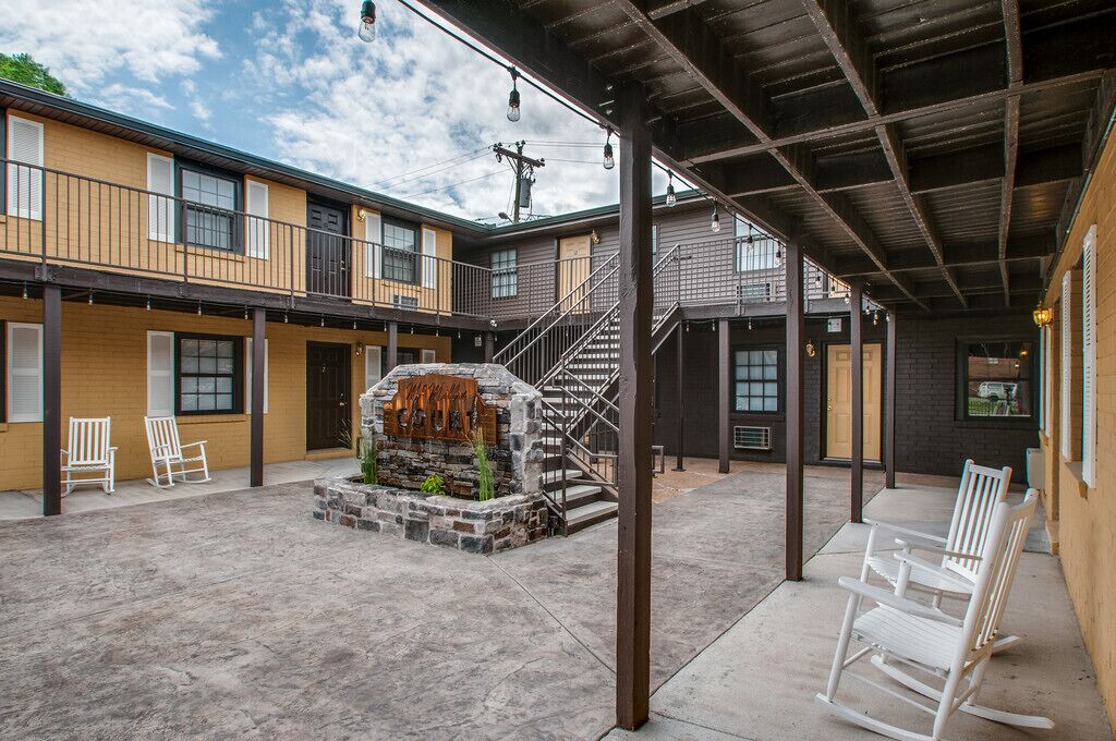Un patio con un hogar de piedra, sillas mecedoras blancas y una escalera que conduce a un nivel superior.