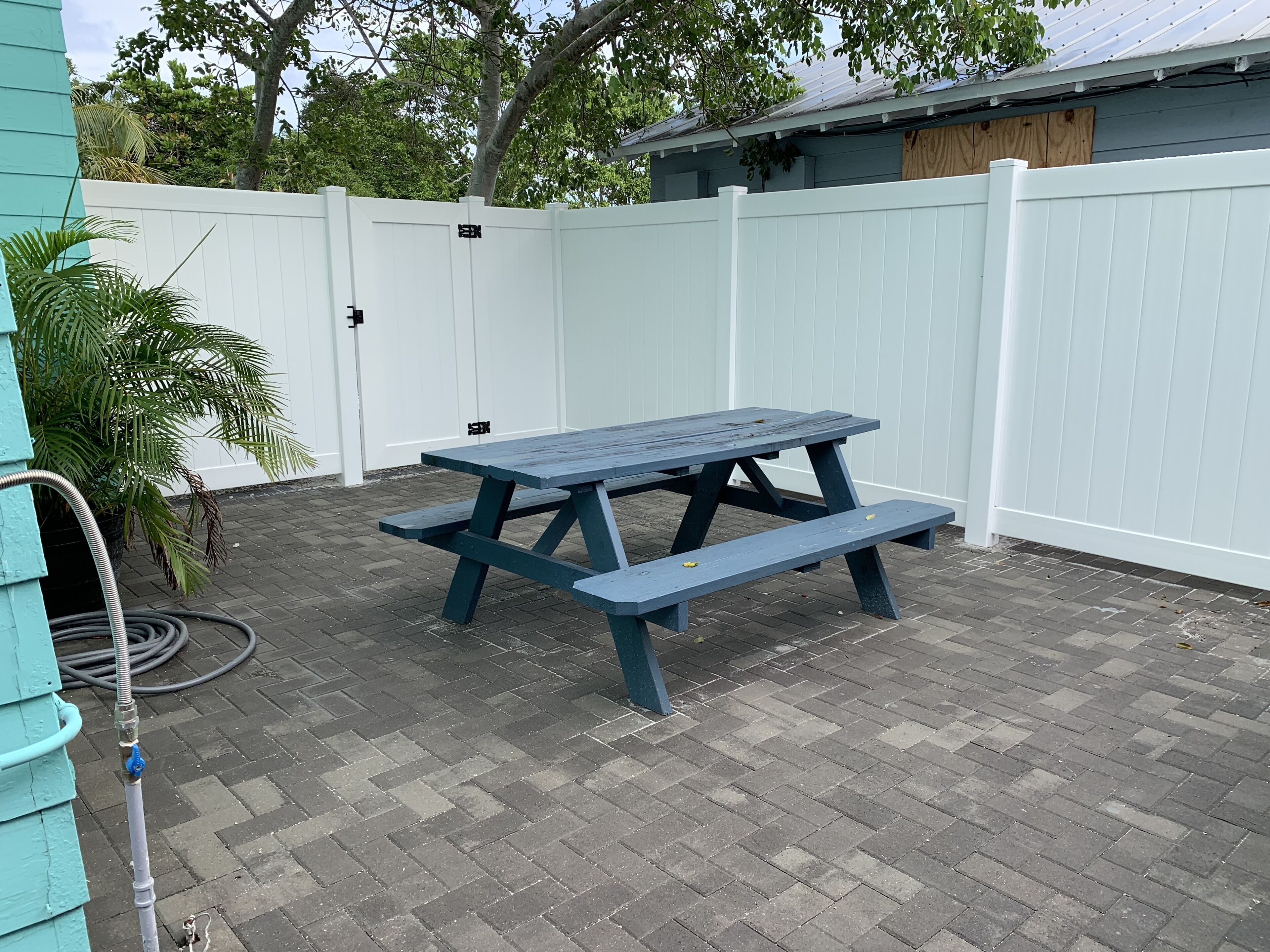 A picnic table in a backyard with a white fence and a house in the background.