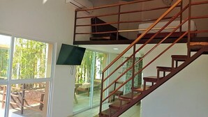 Un interior moderno con una escalera de madera, un televisor de pantalla plana montado en la pared y vistas a un espacio exterior con plantas.