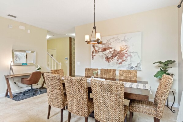 A dining area with a large table, woven chairs, a chandelier, and a large abstract painting on the wall. - Spacious Vacation Home with Pool & Spa Near Disney (Kissimmee)
