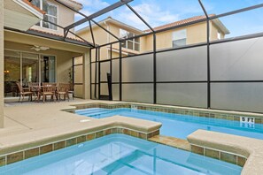 Una piscina con cerramiento de vidrio, un área de patio con sillas y vistas a edificios cercanos.