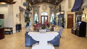 Een ruime lobby met een centraal receptiegedeelte, plantenbakken en een groot decoratief plafond.
