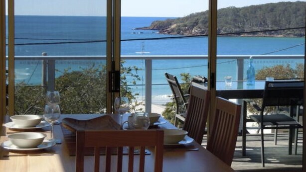 A dining table with chairs and a view of the sea through large windows.