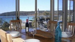 A dining table with chairs, a wine bottle, and a glass, set against a scenic view of a lake and hills.
