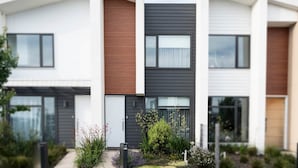 Un edificio residencial moderno de dos pisos con fachada blanca, un panel de listones de madera y una sección gris oscuro.