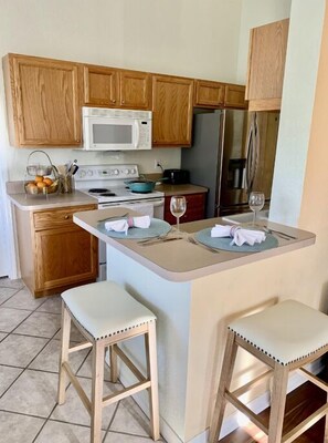 Compact kitchen with island, microwave, refrigerator, stove, and seating for two.