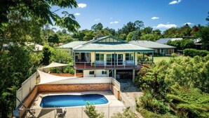 Una casa a due piani con piscina, immersa nel verde e alberi.
