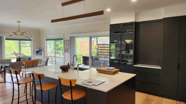 Una cucina moderna con isola centrale, sgabelli da bar e un armadietto nero con bicchieri.