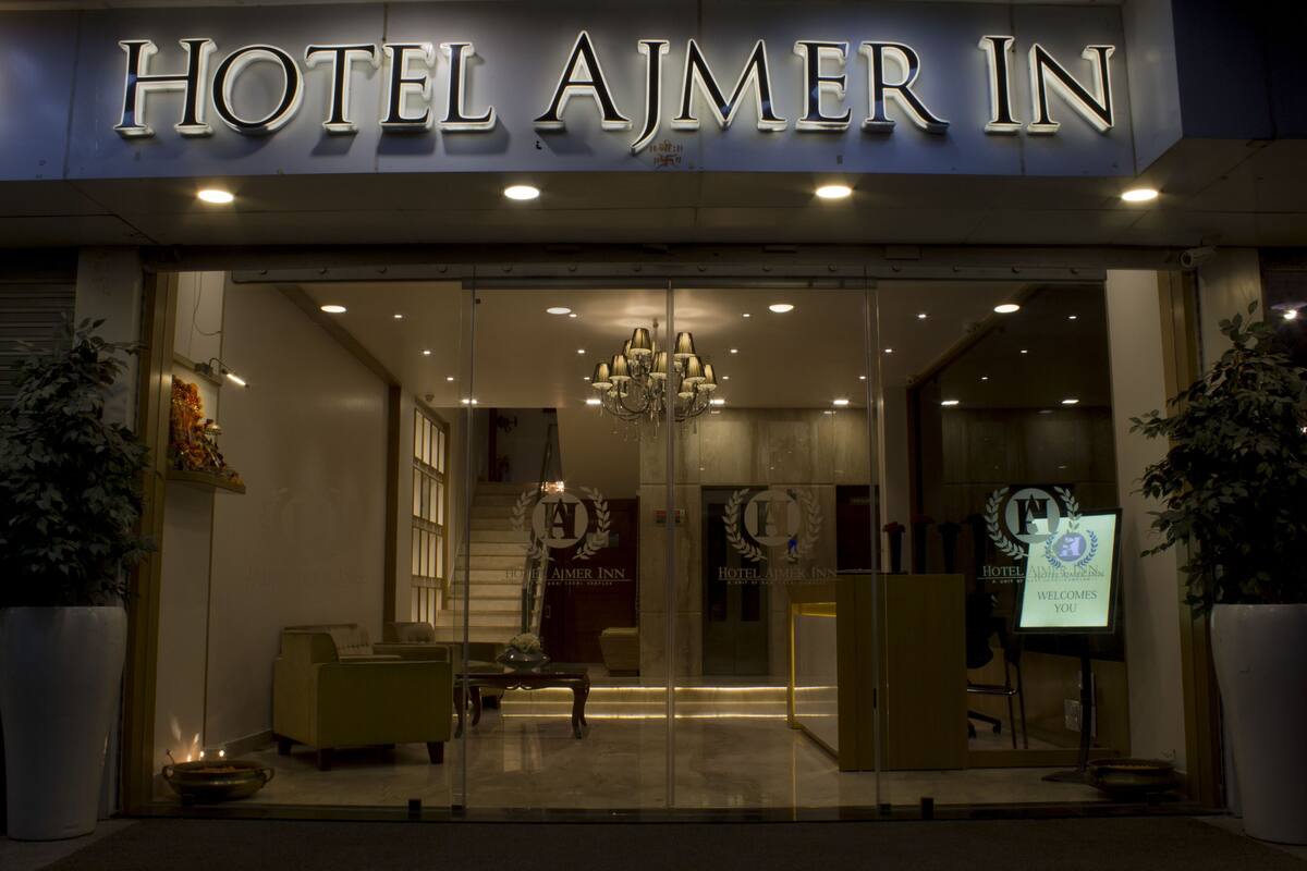 Ein Hotel Eingang mit einem Schild, auf dem 'HOTEL AJMER IN' steht, einer Kristallleuchter und einem Empfangsbereich.