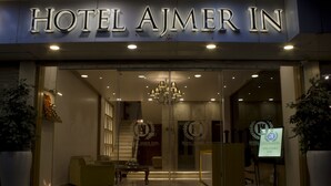Entrada de un hotel con un cartel que dice 'HOTEL AJMER IN', una araña y una recepción.