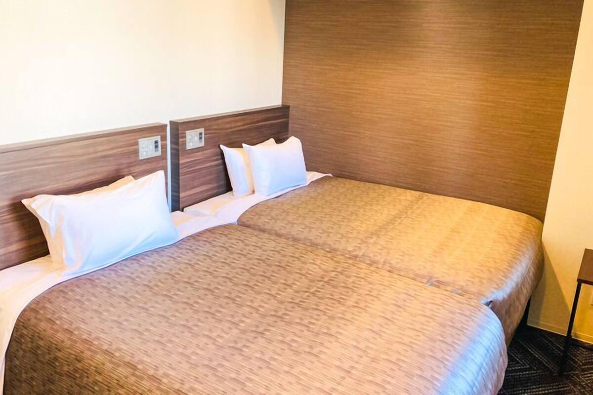 A double bed with a wooden headboard, white bedding, and a carpeted floor.