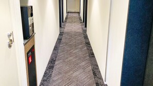 Ein Hotelgang mit Teppichboden, einem Rauchmelder links und einer blauen Tür rechts.
