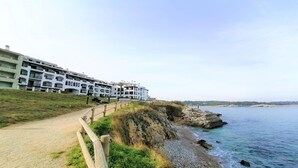 Un hotel frente al mar con varios balcones, una playa de arena y un litoral rocoso.
