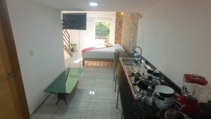 A compact kitchen with a dining table, a bed, and a TV mounted on the wall. - PALMAS DE CHAHUE C (581 SF) (Crucecita)
