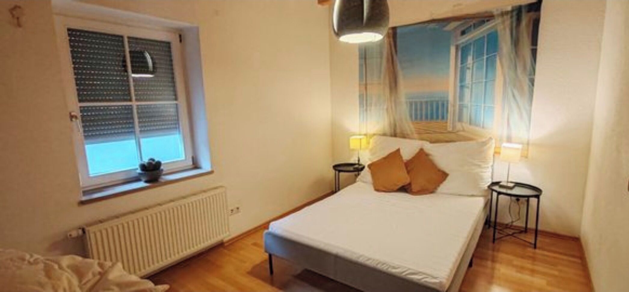 A bedroom with a bed, a window with blinds, a radiator, and a lamp.