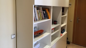A white bookshelf with books and a mug, a door, and a light switch.