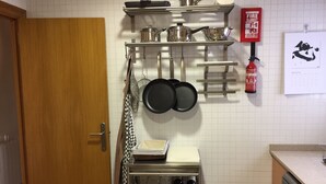 A kitchen with a wooden door, a metal rack holding pots and pans, a fire extinguisher, and a calendar on the wall.