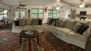 Ein geräumiges Wohnzimmer mit zwei beigefarbenen Sofas, einem Couchtisch und einem großen Fenster mit Blick ins Freie.