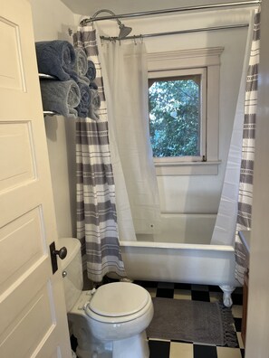 A bathroom with a bathtub, toilet, and a window with a view of trees. - The Barlow (Hotchkiss)