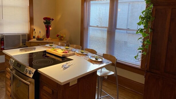 Una cocina moderna con una isla central, horno empotrado y un amplio ventanal con persianas.