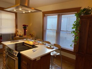 Een moderne keuken met een centraal eiland, een ingebouwde oven en een groot raam met zonwering.