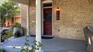 Una casa de ladrillo con puerta roja, columnas blancas y un cartel con un número en la pared.