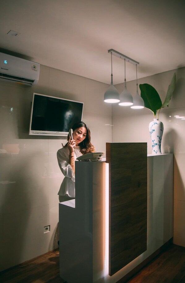 A reception desk with a flat-screen TV, a potted plant, and pendant lighting. - Deva Bali Apartment (Kerobokan)