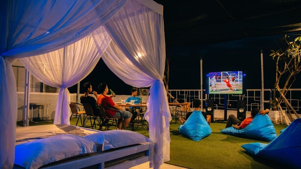 A bed with a canopy, a TV screen, and people sitting on bean bags. - Deva Bali Apartment (Kerobokan)